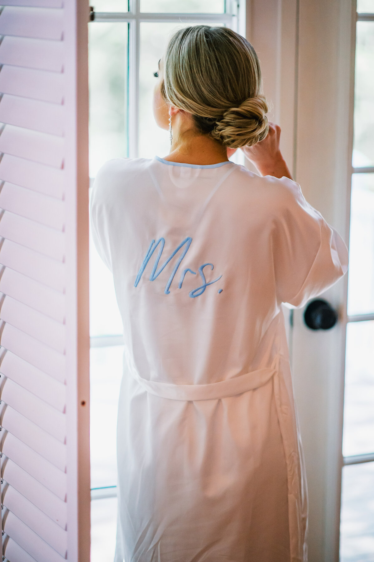 Bride wearing embroidered “Mrs.” robe getting ready by the window at Old Edwards Inn wedding in Highlands, North Carolina.