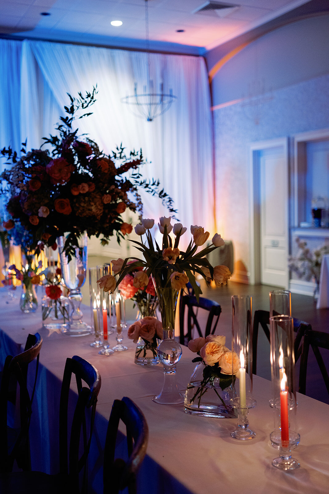 Long reception table at Burritt on the Mountain adorned with vibrant floral arrangements, flickering candles, and romantic uplighting in warm and cool tones.