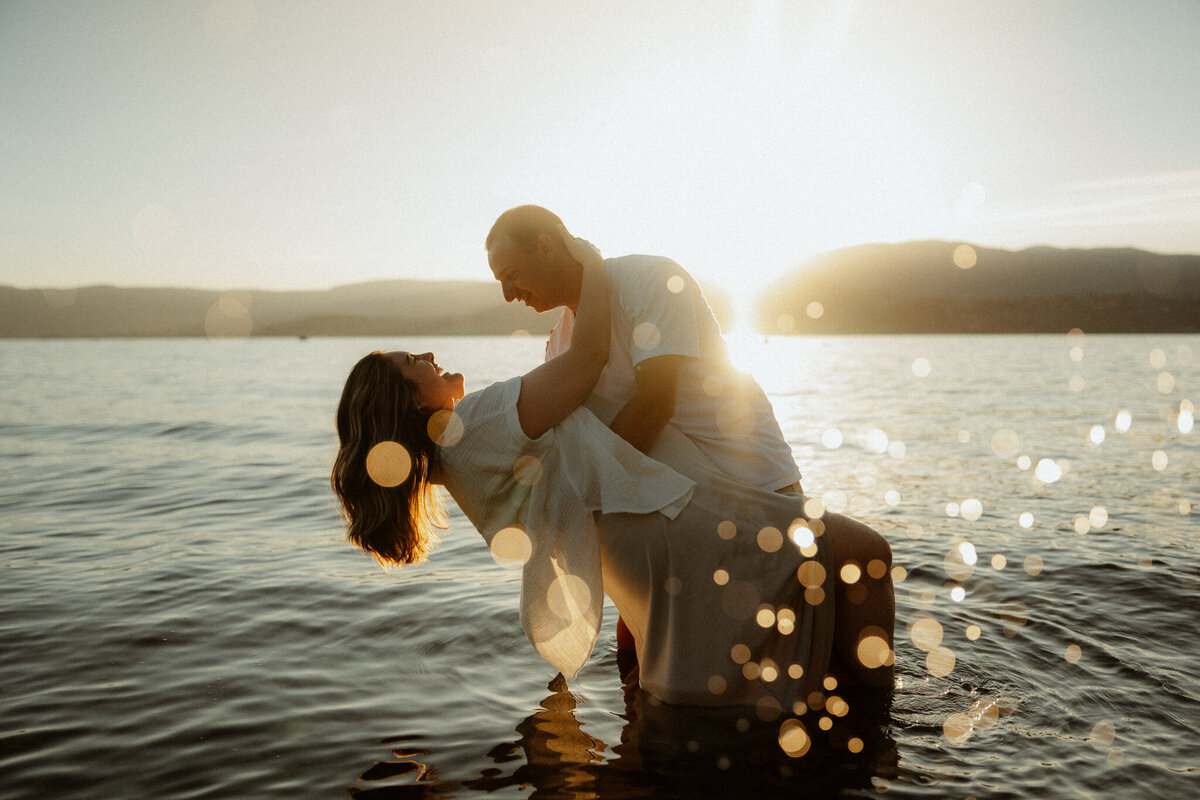 A couple standing in the water at a kelowna beach during a golden sunset with water splashing