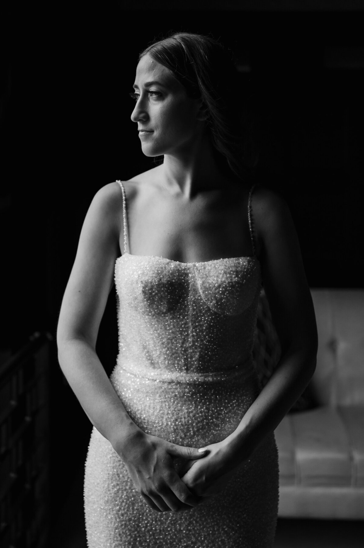 A moody bride wearing a dress with pearls stares out the window at Revel Motor Row