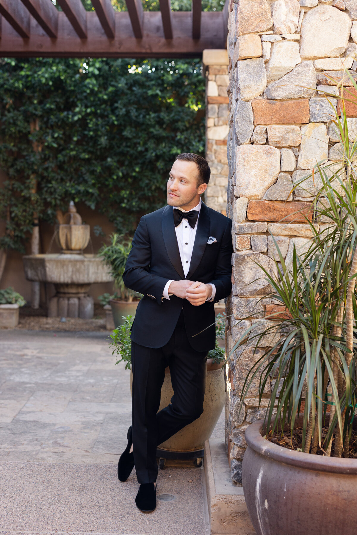 Groom leaning on wall posing for portrait on wedding day in Arizona