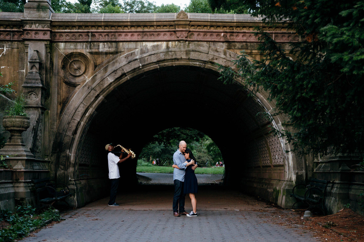 a couple hugging while standing in front of a small bridge.