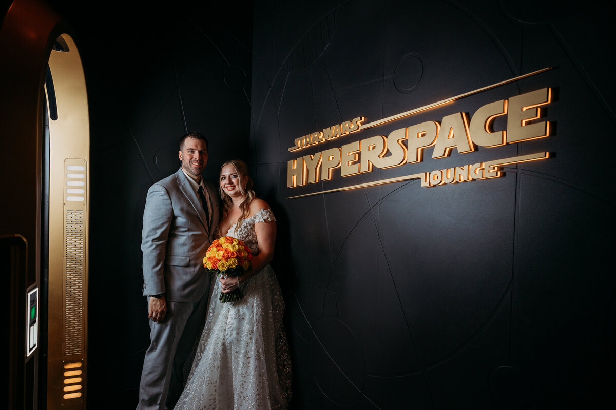Wedding couple poses with bouquet in front of Star Wars Hyperspace Lounge signage aboard the Disney Wish cruise ship.