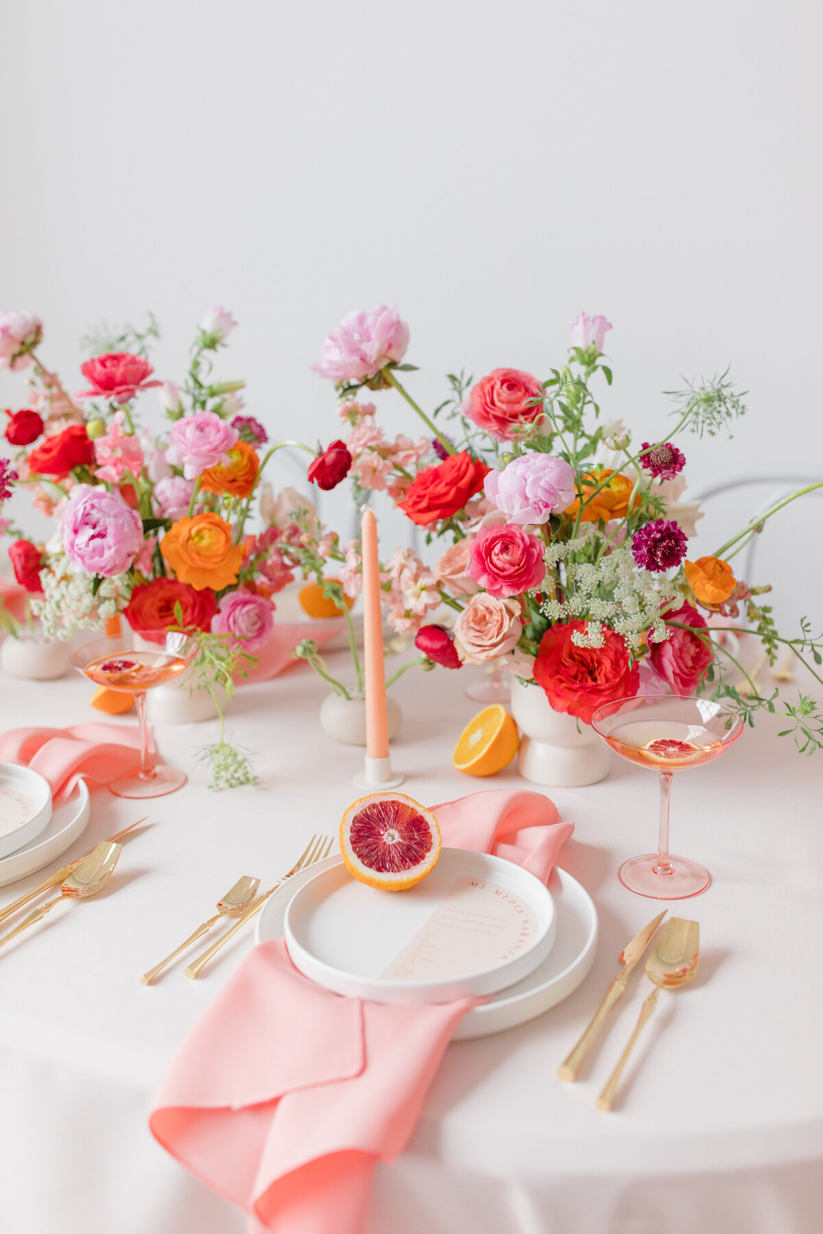 wedding table place setting with bright colorful florals, pink candles, pink napkins