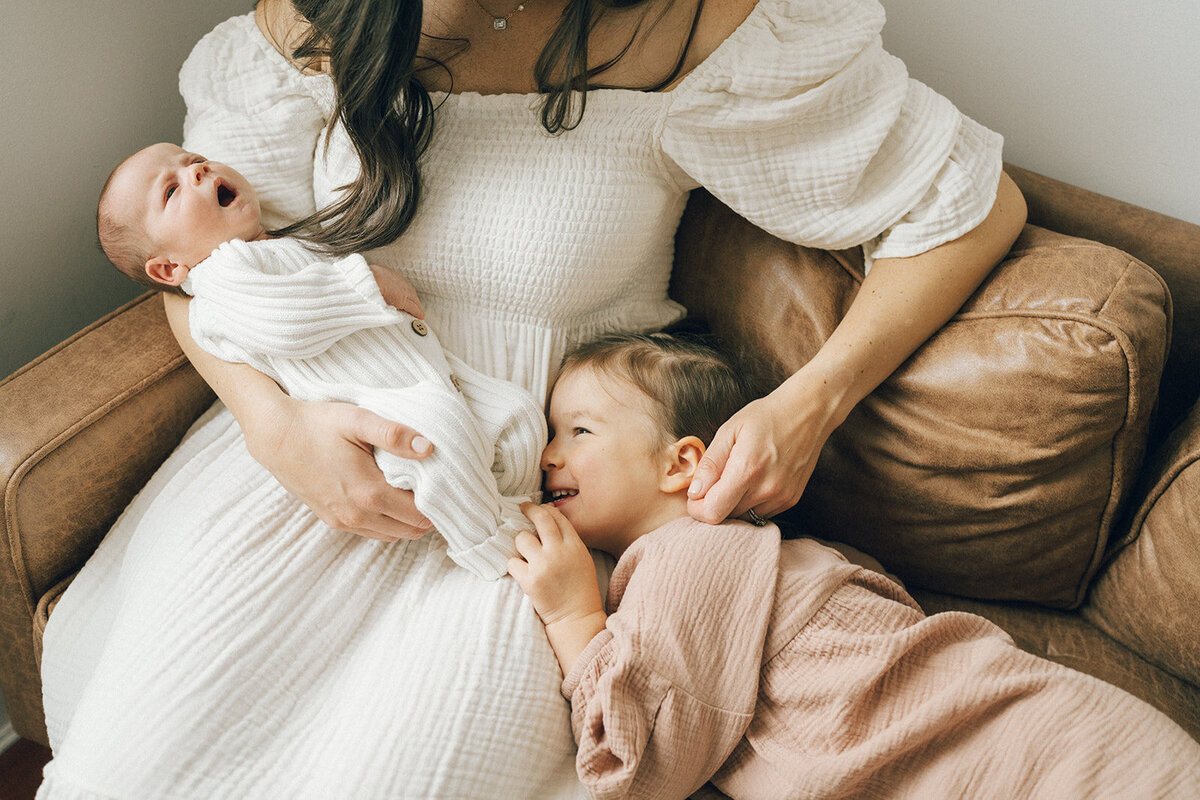 Mom gently touching her daughter’s ear while cradling her newborn baby during a cozy in-home session