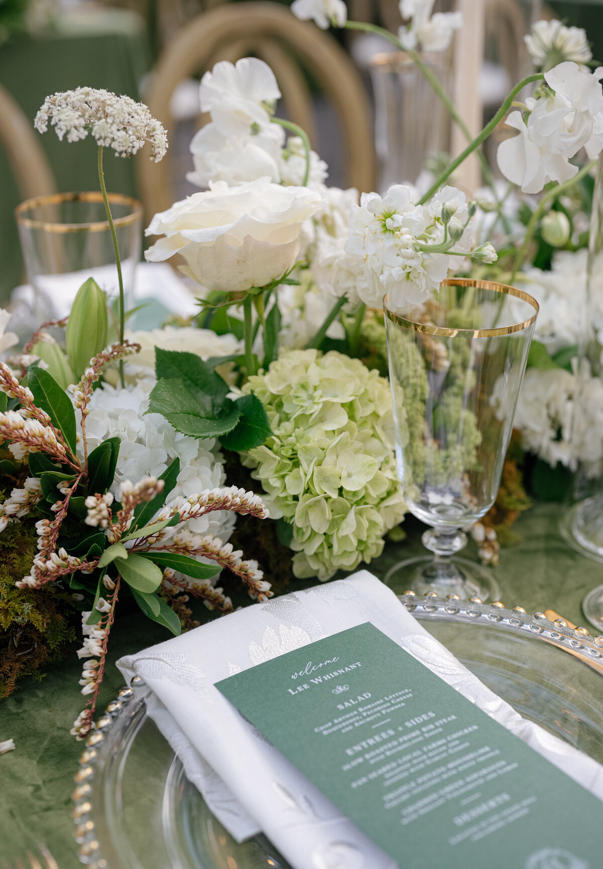 Detailed floral arrangement with white roses, hydrangea, and soft greenery as part of an elevated wedding centerpiece.