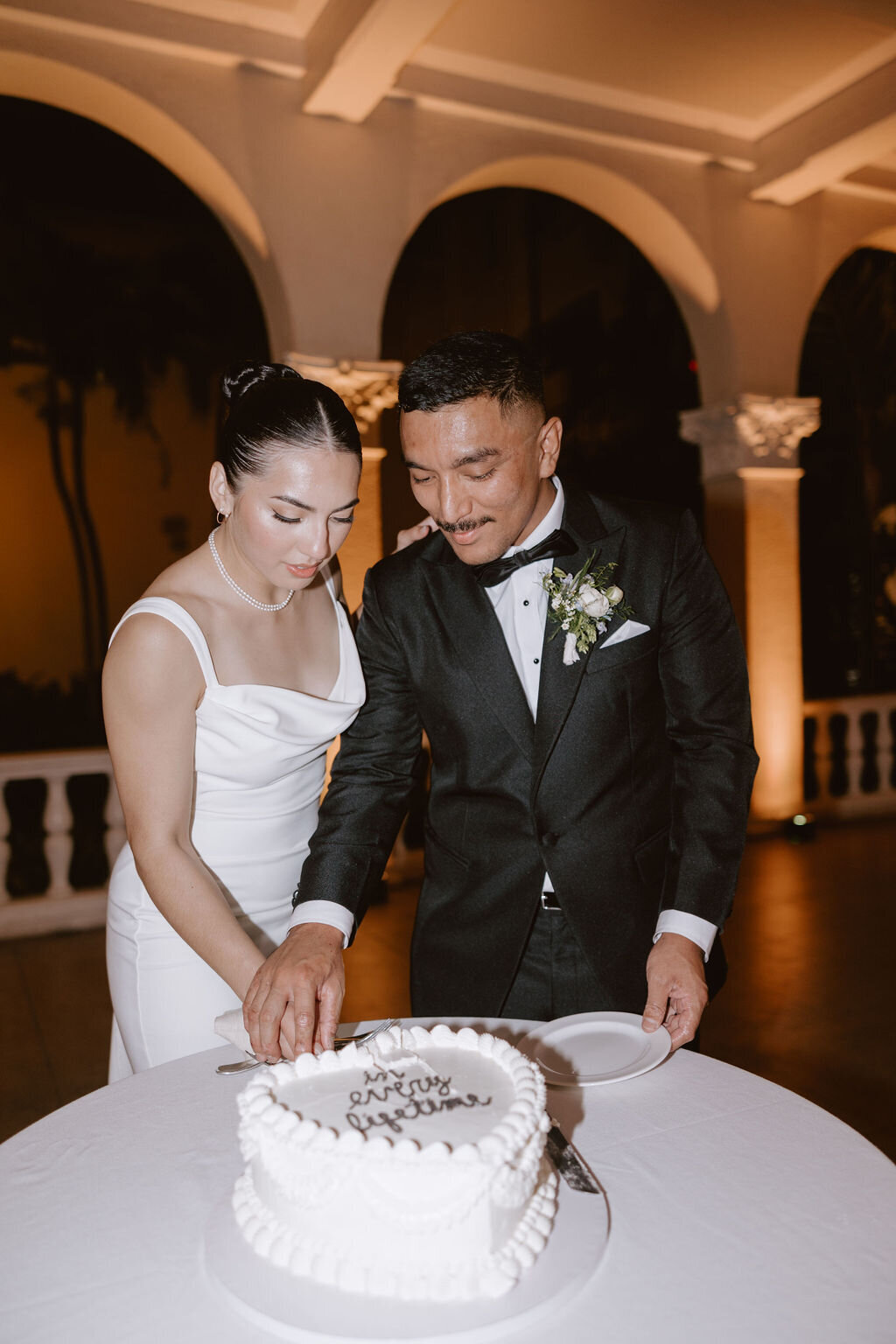 Brid eand groom cake cutting with vintage heart one tier cake and european arches behind them