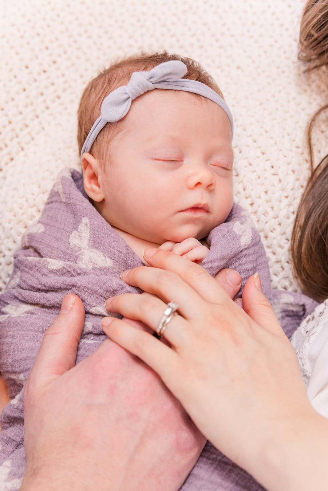 mum and dad hands covering newborn baby sleeping on a bed