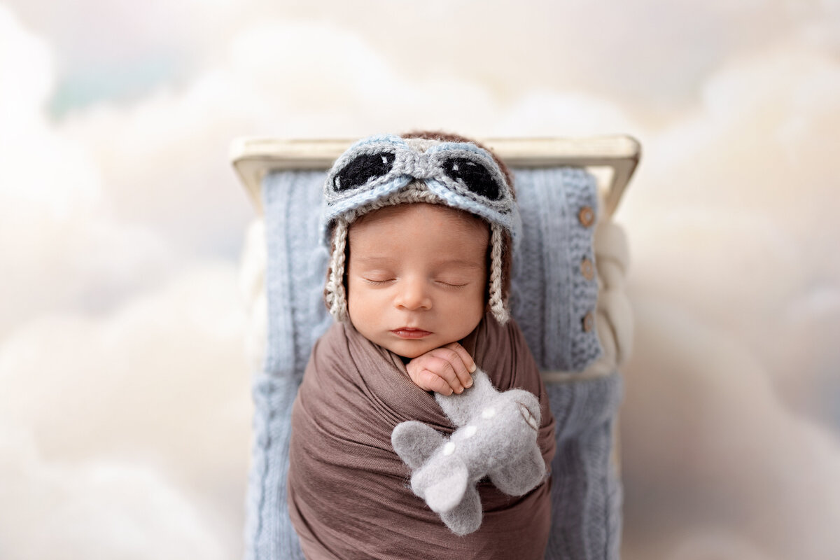 Milton newborn photography session featuring baby boy in aviator hat and goggles curled in a rustic wooden prop.
