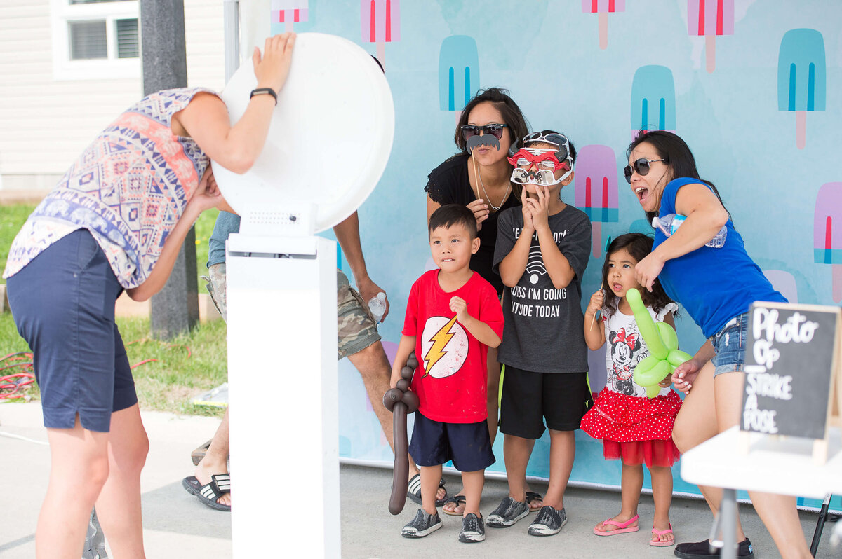 two moms and their young children enjoying a photobooth of props during a corporate children's event.  Captured by Ottawa Event Photographer JEMMAN Photography COMMERCIAL
