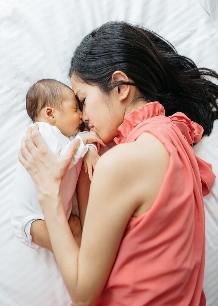 Mother and her baby lying down together, with their heads touching in a tender moment.