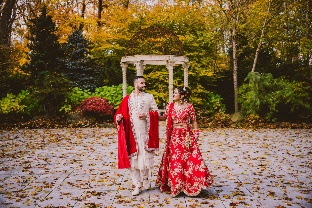 An indian wedding couple walking down a path with fall leaves during their hindu wedding at crystal plaza nj