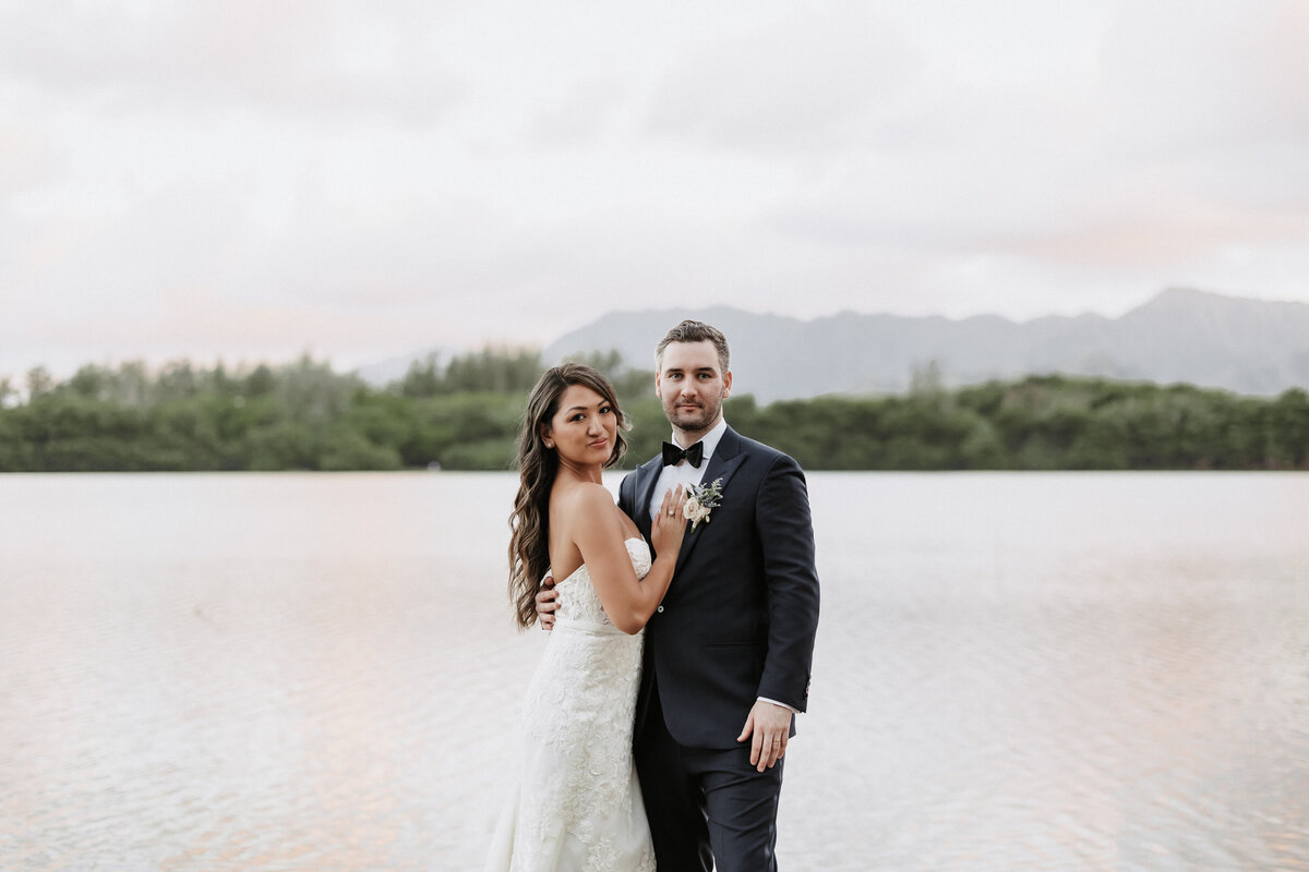 Wedding couple with water in the background and horizon of trees