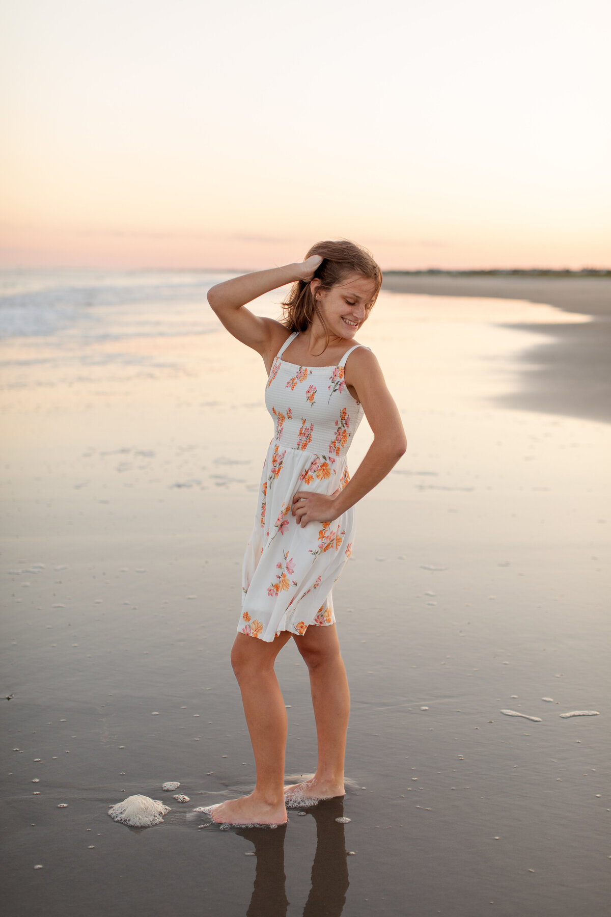 Senior stands in the sand, left hand on her hip, right hand running through her hair