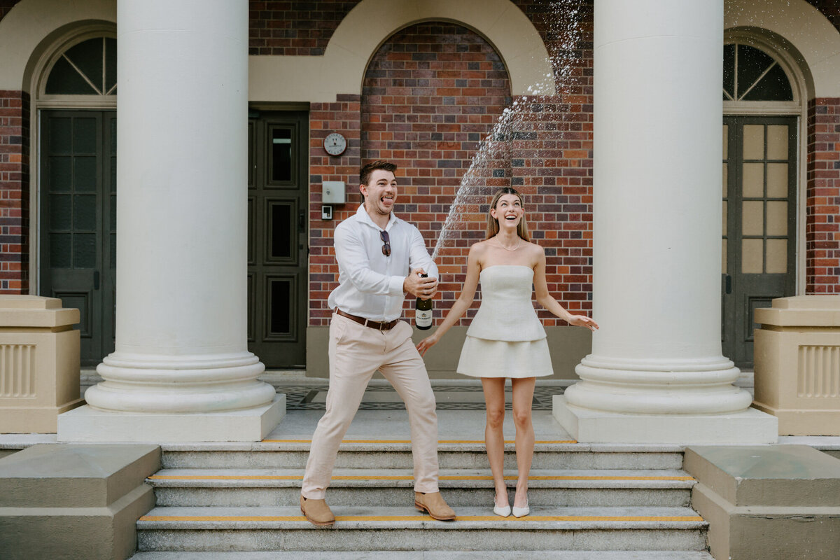 engaged couple spraying champagne on art gallery steps
