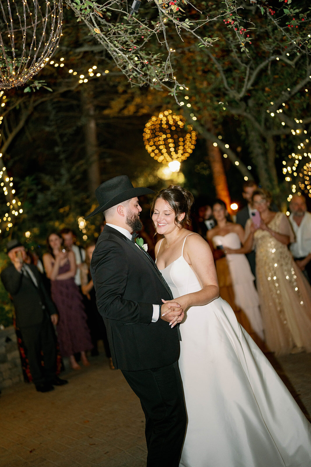 Bride and groom dancing surrounded by wedding guests at Café Cortina reception, romantic evening wedding photography.