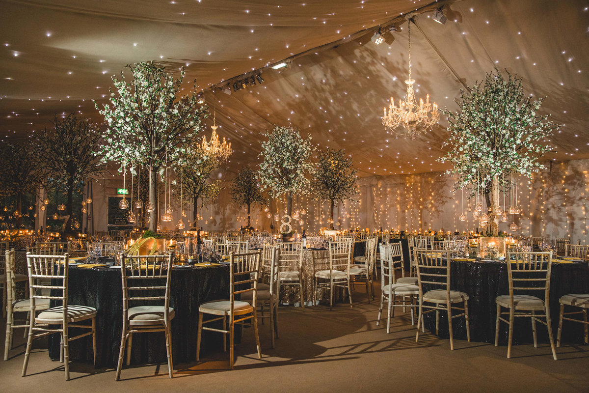 The marquee at Iscoyd Park set up in winter for a intimate wedding breakfast with flowers and trees on the table by red floral architecture