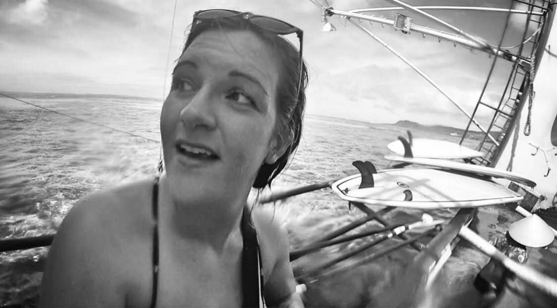 Nicole looks past camera on a boat in the open sea with paddle boards in the background.