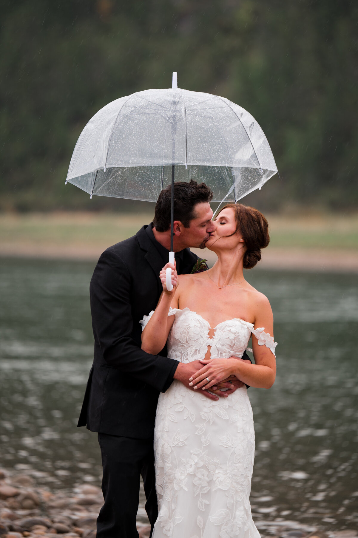 Edmonton, Alberta wedding photography featuring a bride and groom kissing, holding an umbrella to sheild themselves from the rain
