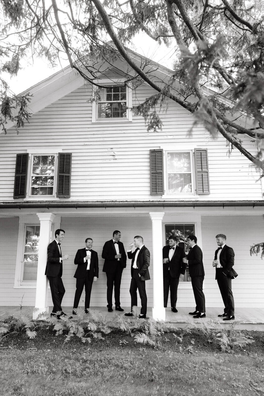 The groom and groomsmen are chatting while drinking brandy outside the guest house at Lion Rock Farms, CT. Image by Jenny Fu Studio