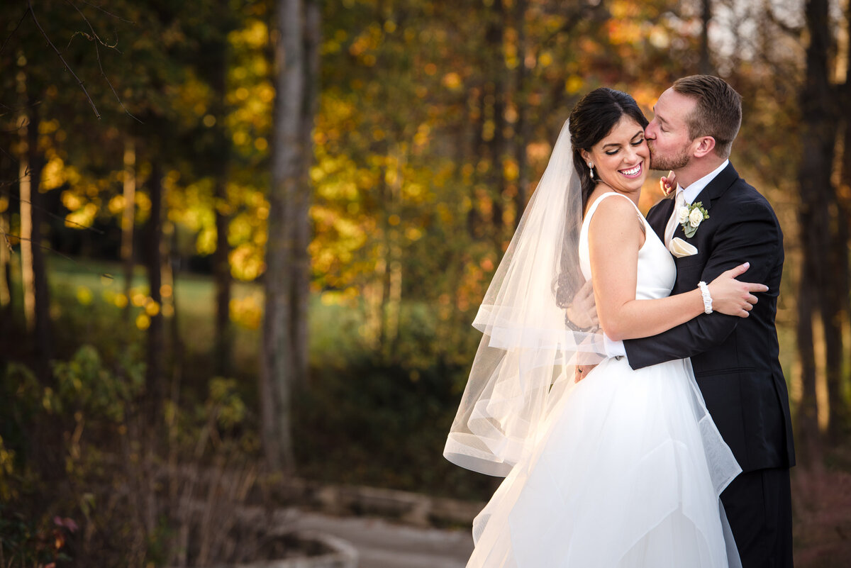 Groom kissing bride's cheek on the course during golden hour at Trump National Golf Club by Charlotte wedding photographers DeLong Photography