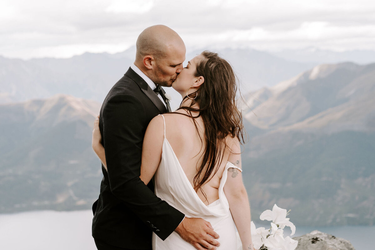 The Lovers Elopement Co - bride and groom kiss at wedding ceremony on top of mountain in New Zealand
