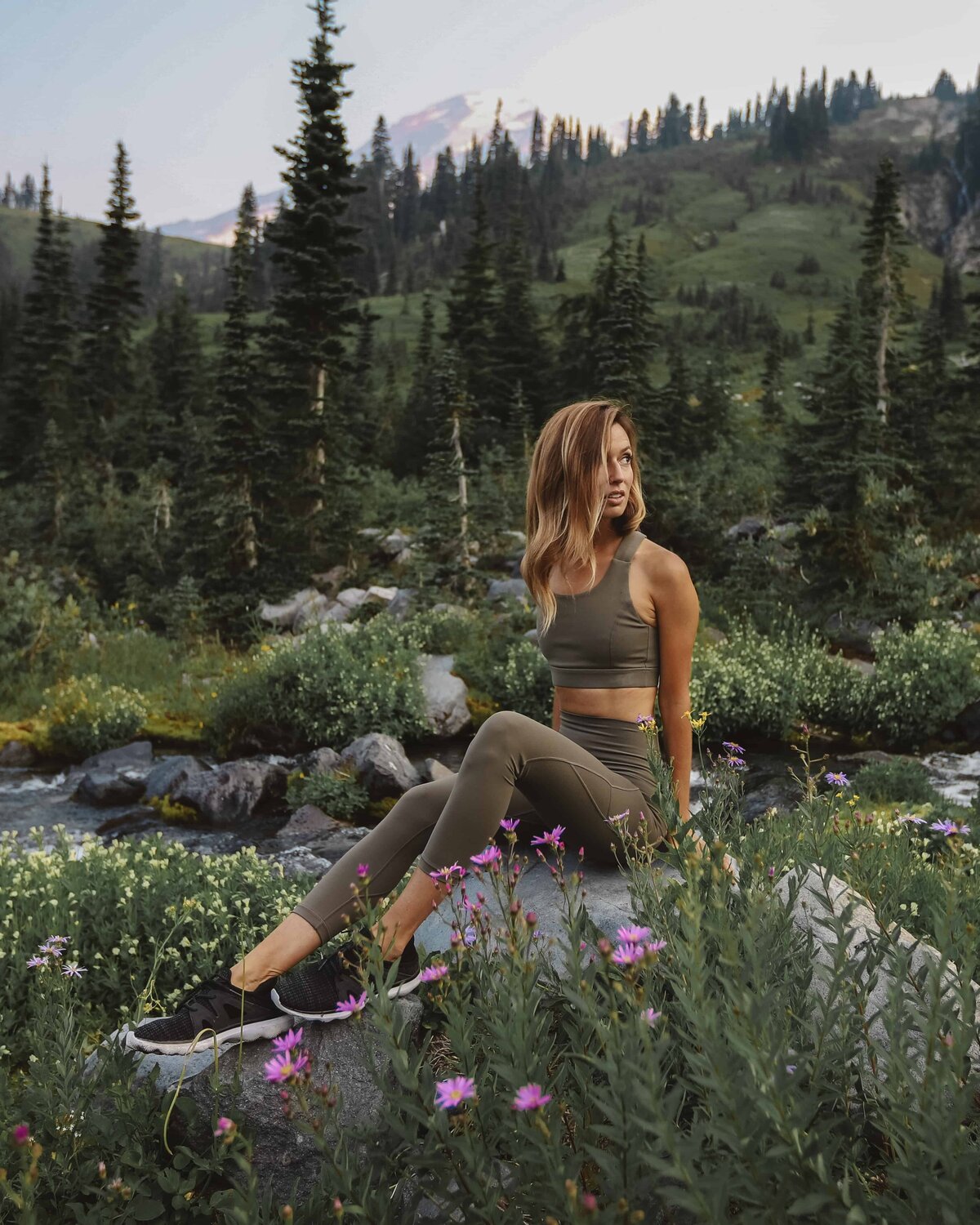 Jess of Jess Wandering wearing brown Glyder Apparel outfit sitting on a rock by wildflowers and trees