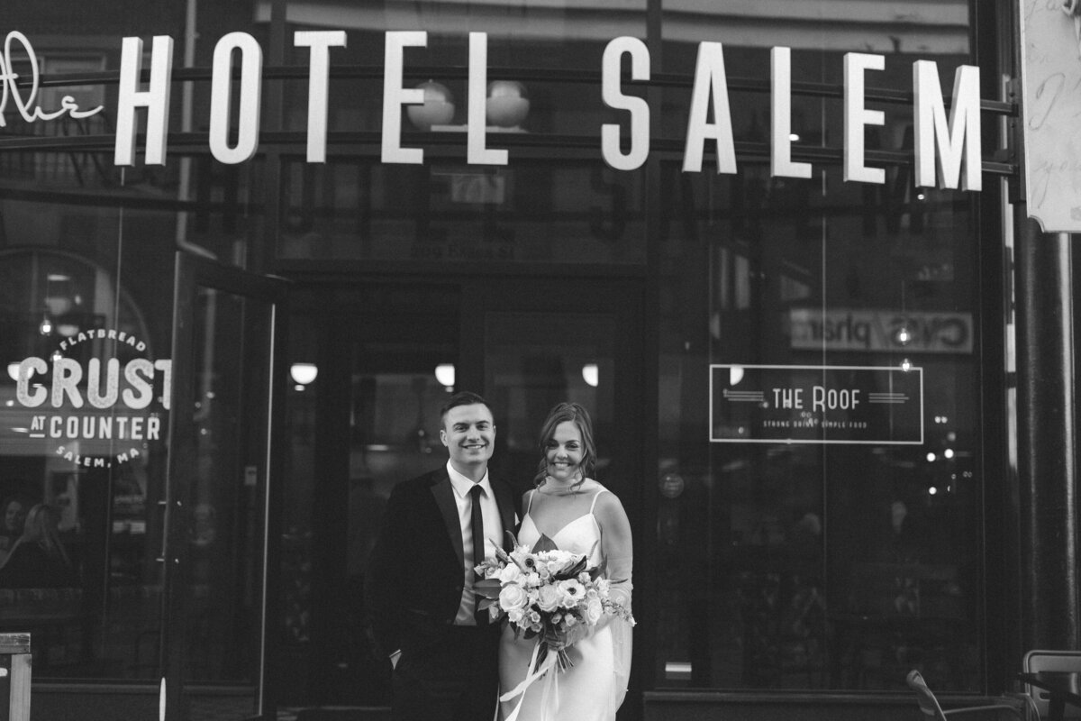 A bride and grrom standing in front of a hotel that says Hotel Salem on the front 