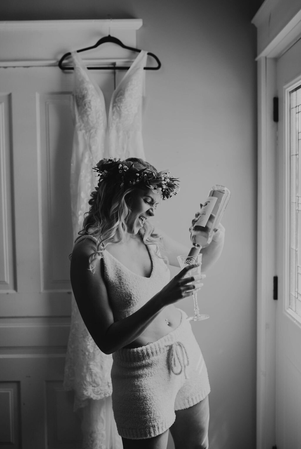 bride is pouring herself a glass of wine as she gets ready for her wedding