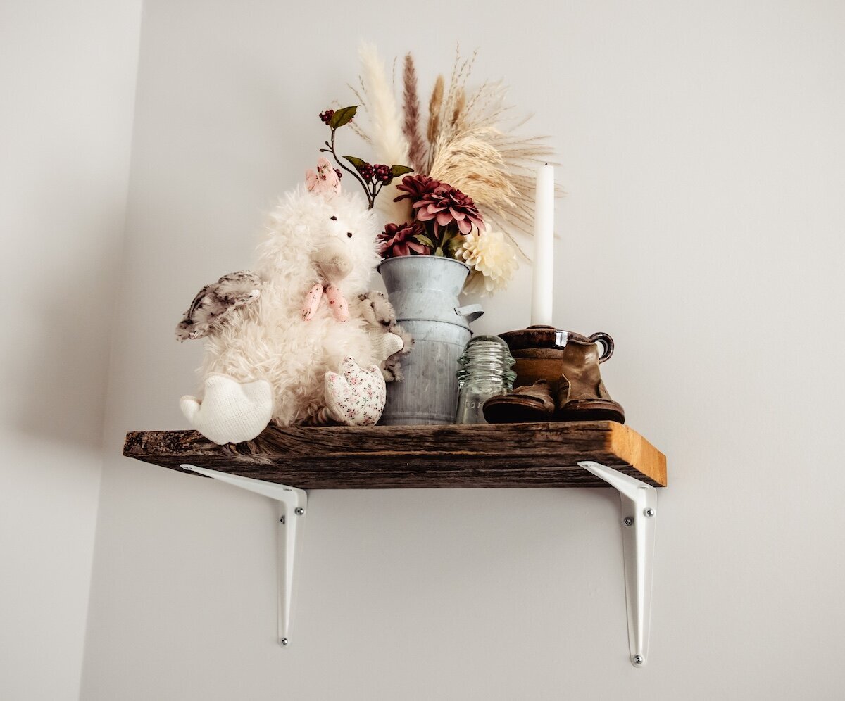 A shelf in a nursery of a baby girl with a stuffed animal, flowers, and a candle on it