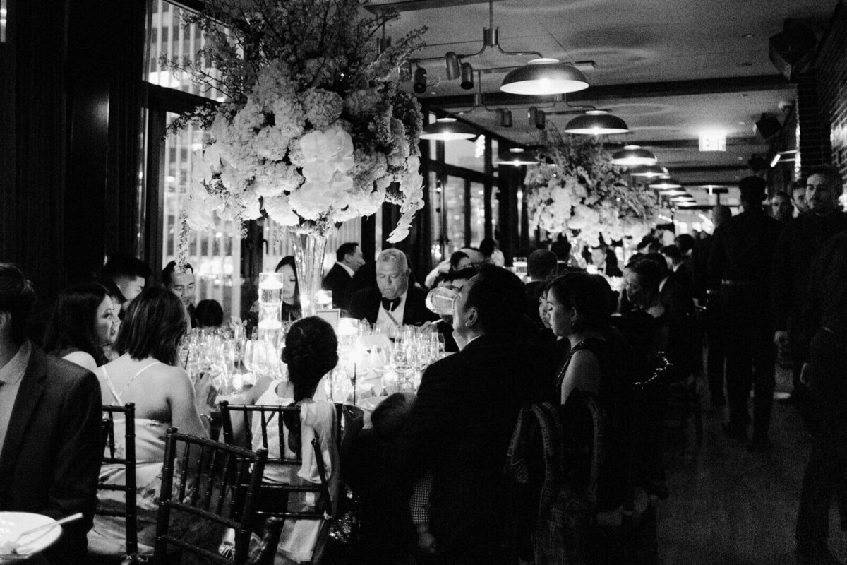 Black and white photo of guests dining in the wedding reception in The Skylark, New York. Wedding Image by Jenny Fu Studio