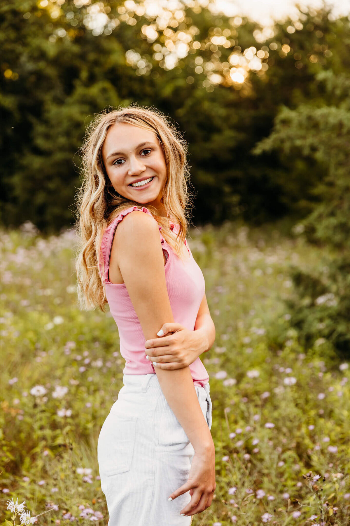 blonde girl in a pink tank top smiling in a field of wildflowers in Oshkosh
