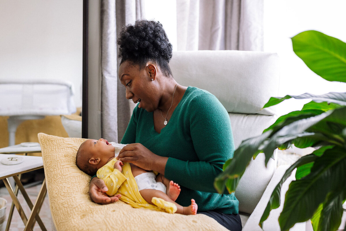 mom in green sweater changing newborn's clothes on pillow on her lap