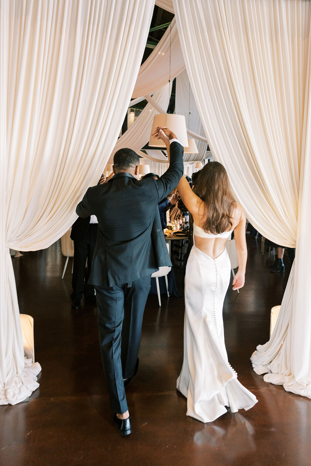 The newlyweds make their entrance into the reception, walking through draped white fabric with hands raised in celebration.