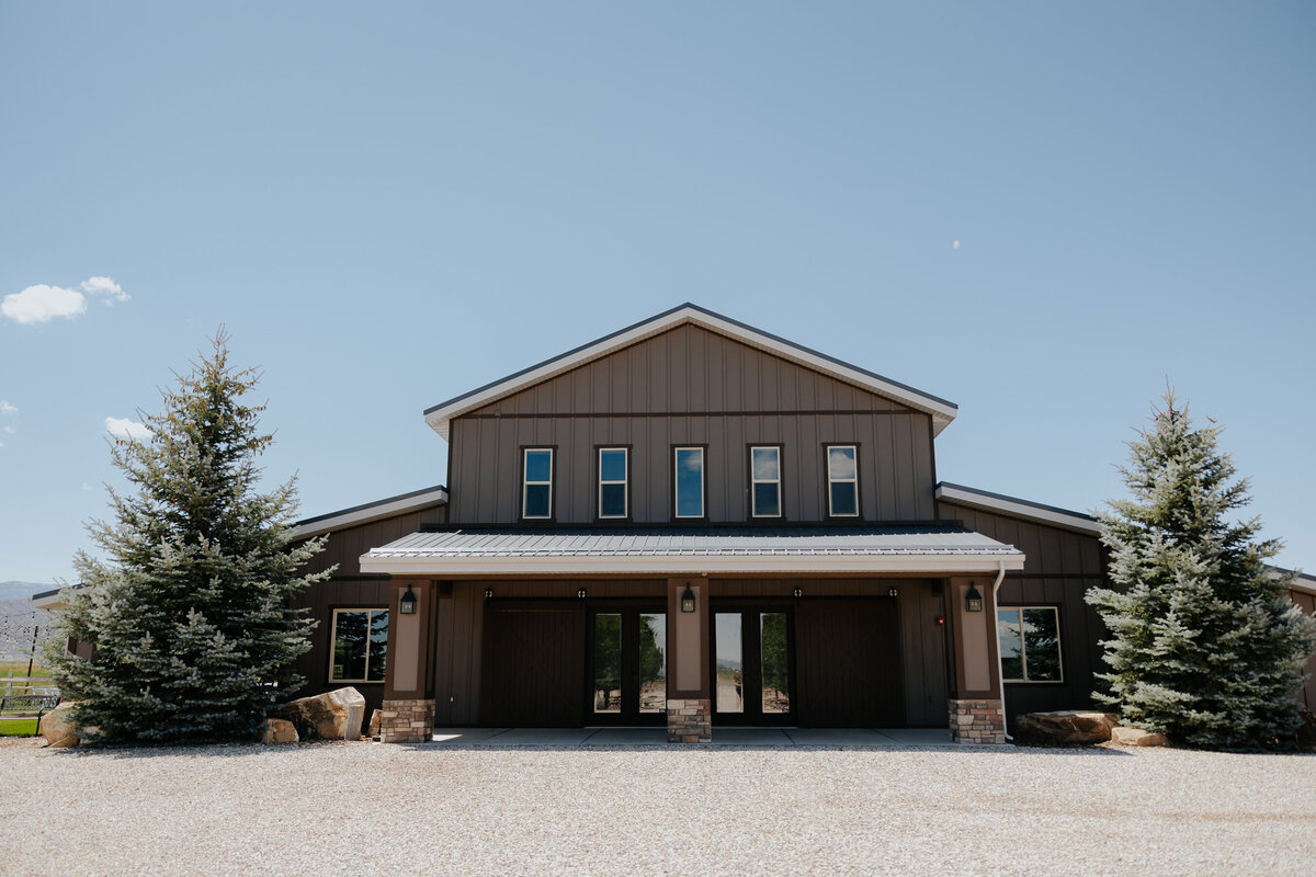 Front of the barn with evergreens and the gravel drive