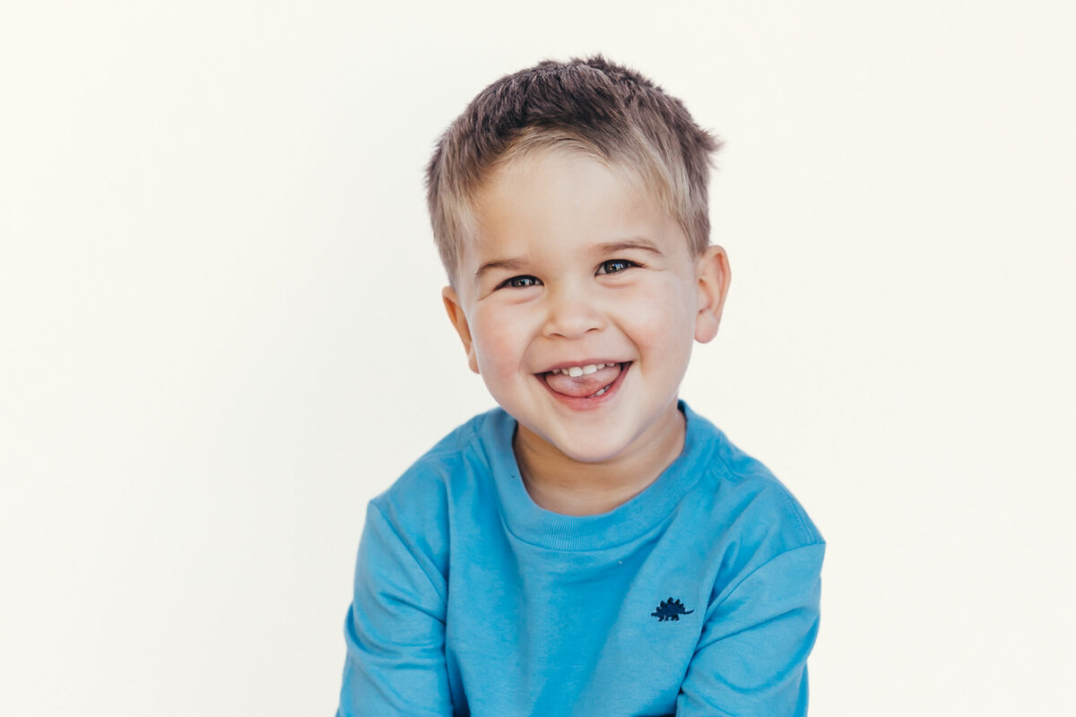 A young boy smiles in front of a white backdrop