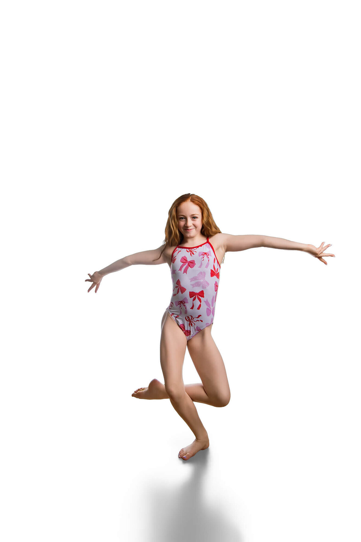 Action Portrait of a young red haired gymnast in a light pink leotard with bows on it on white, taken by las vegas gymnastics photographer