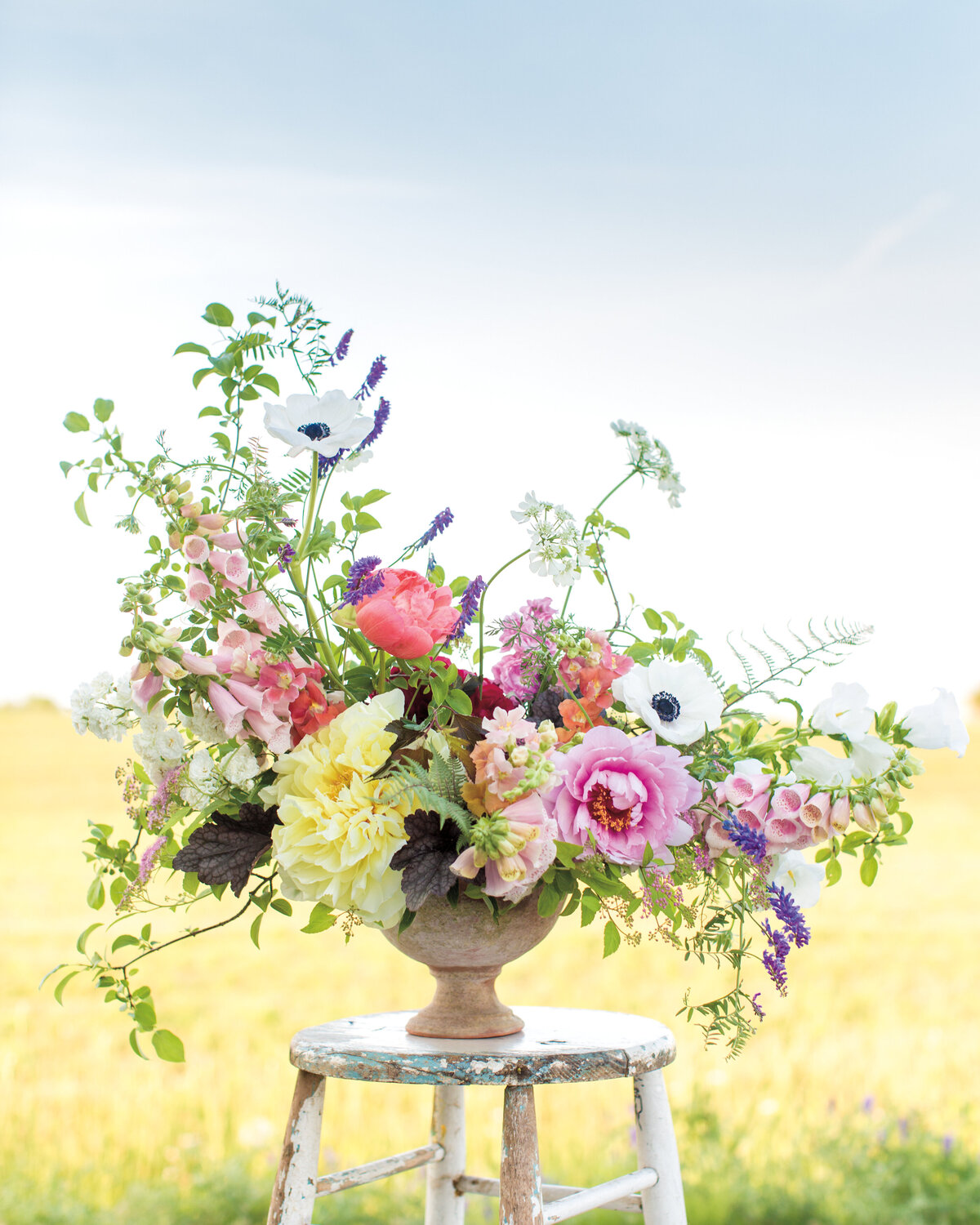 A colourful floral arrangement of spring flowers displayed on a stool in front of a field.