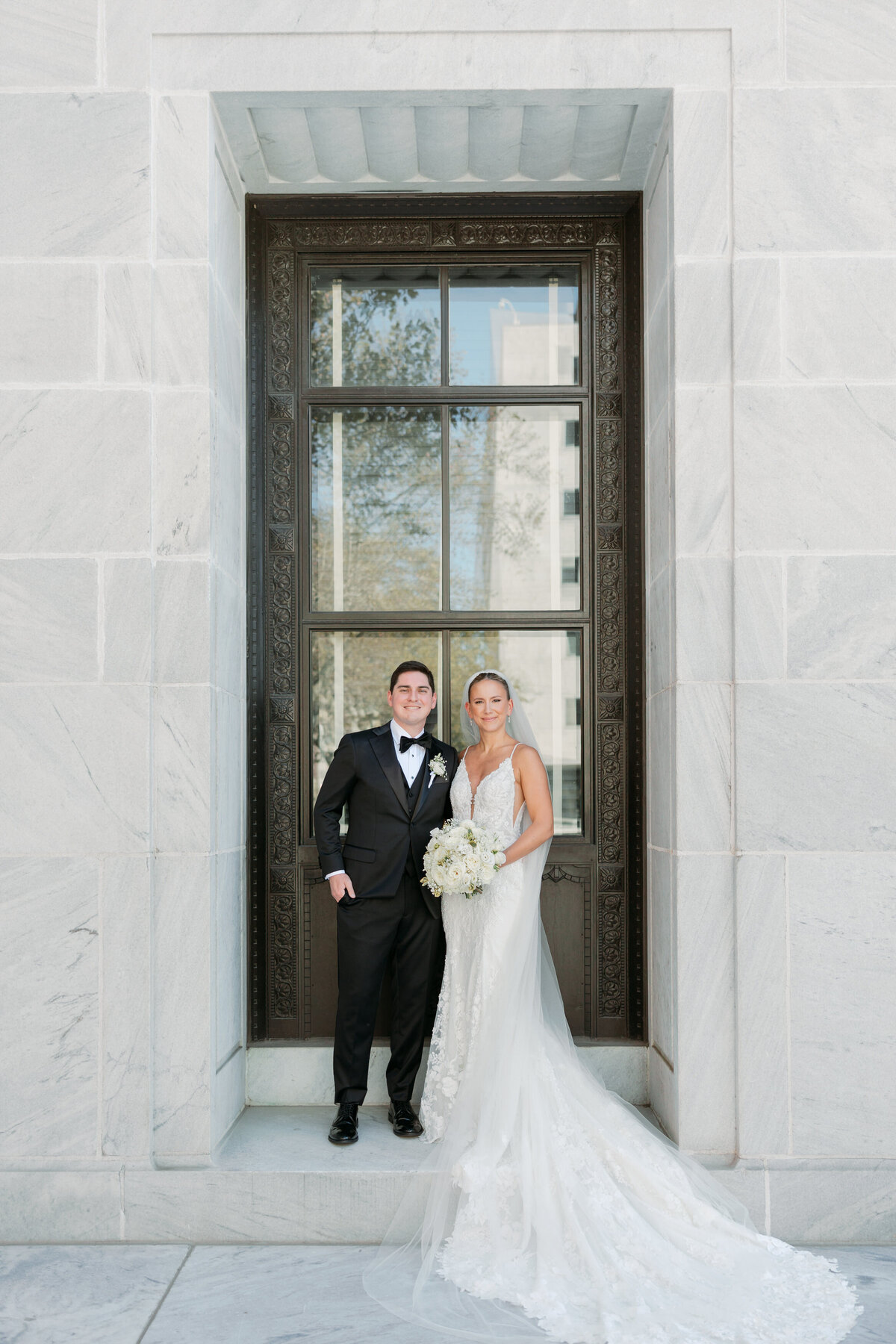Bride and groom pose together in a tall window alcove with stone and iron detailing in Philadelphia.