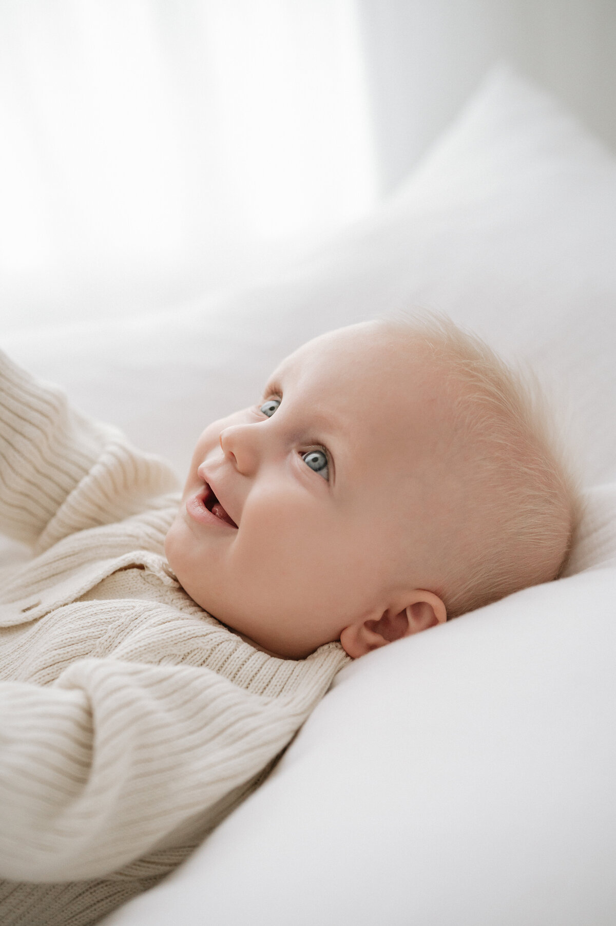 Baby lies on a white cushion smiling up