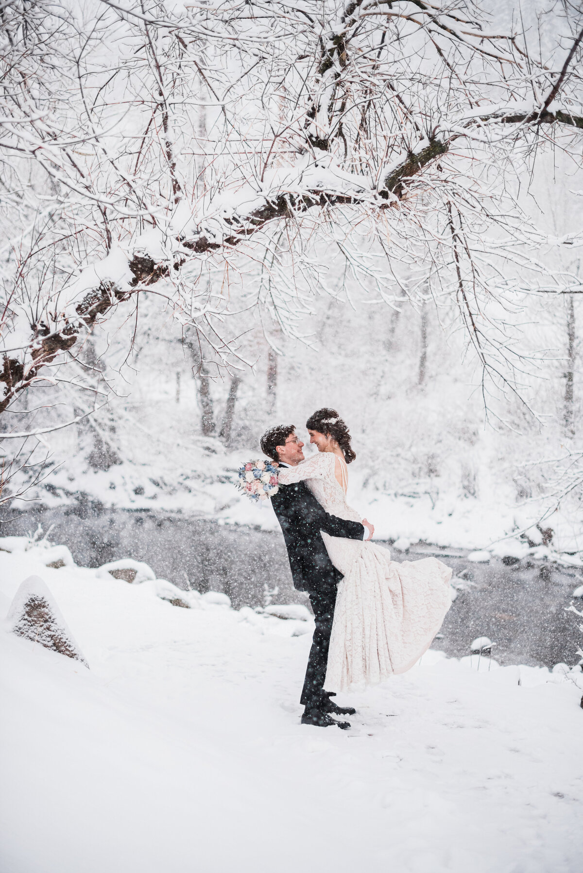 winter wedding photographed by denver wedding photographer in the rocky mountains with bride adn groom dancing in the snow next to a stream with the snow falling around them