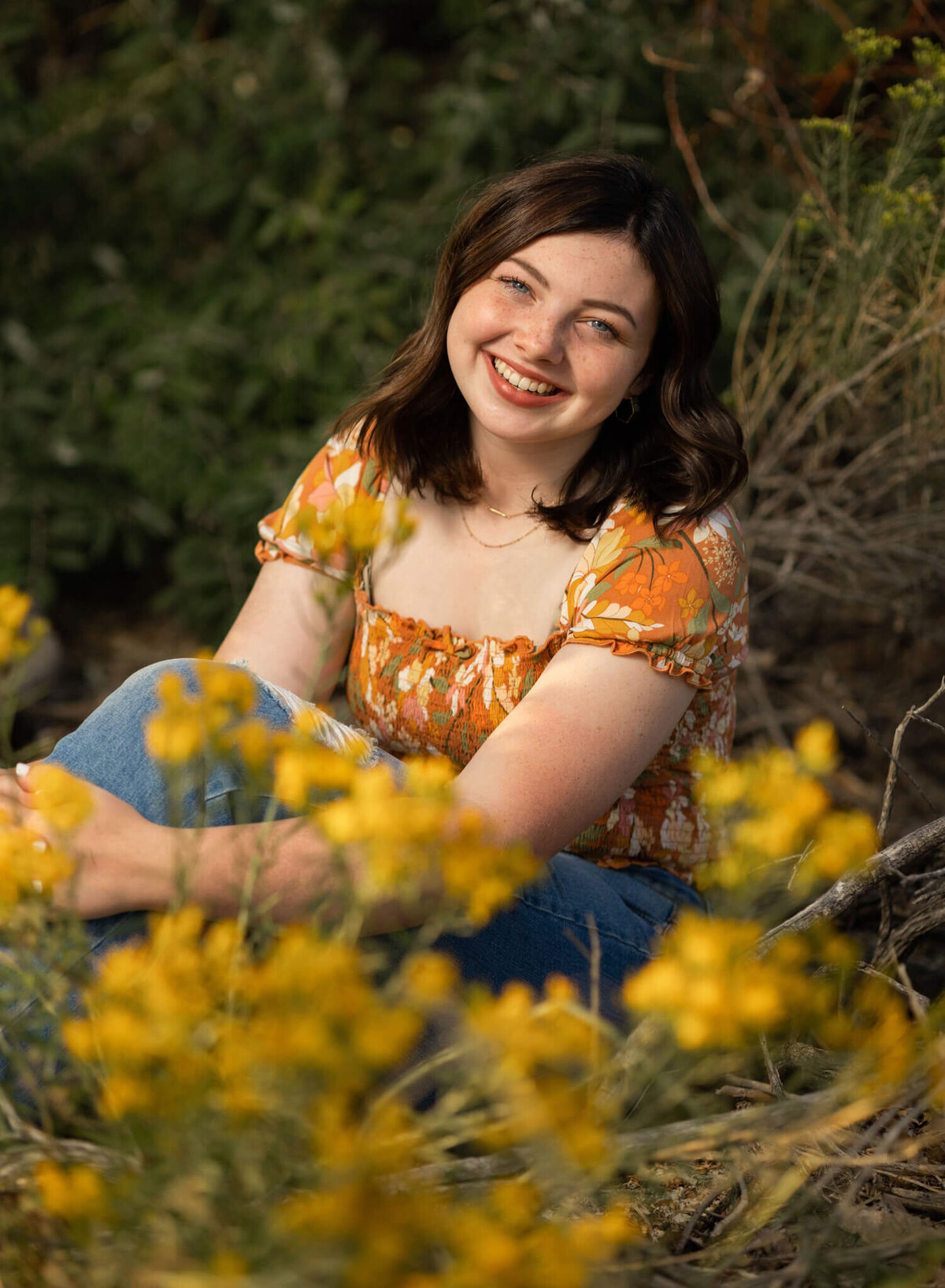 high school senior girl sitting in some grass by small yellow flowers