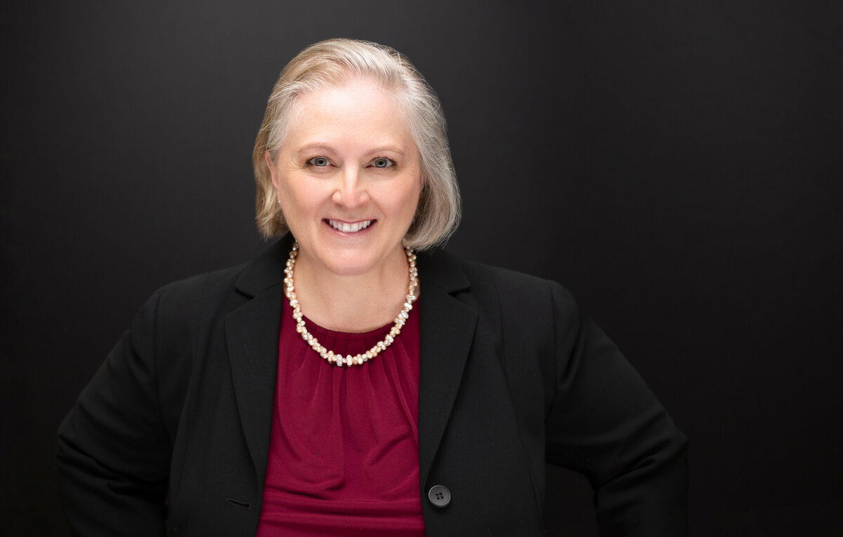 A white female medical professional poses for a business headshot photo on a black background at Janel Lee Photography studios in Cincinnati Ohio