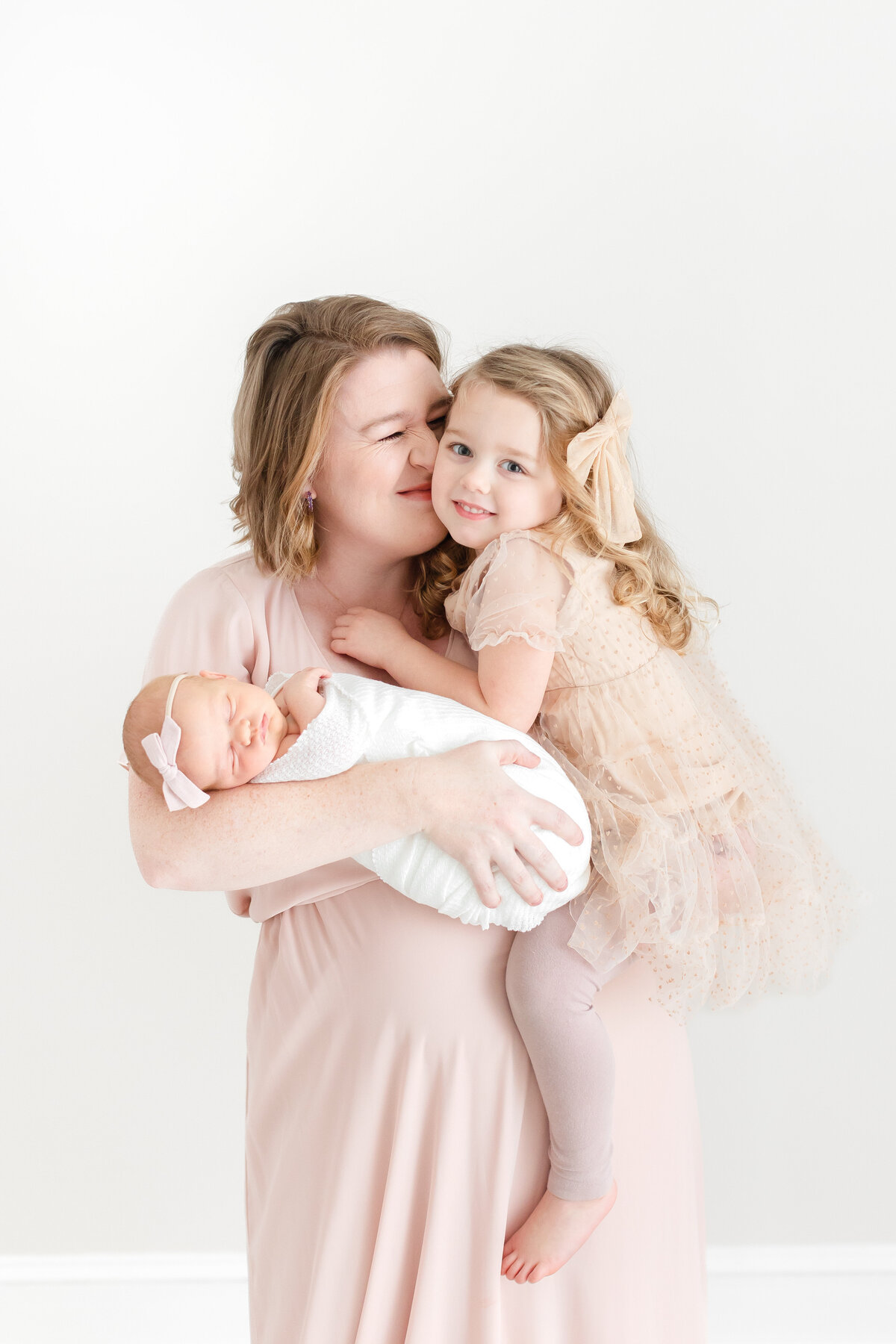 A mother in a pink maxi dress holding her toddler daughter and newborn baby girl at their DC Newborn Photography photoshoot