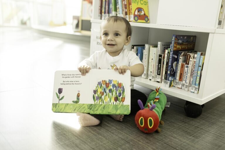 First birthday photoshoot with a baby boy in the library, surrounded by books and soft lighting, giving a sweet smile