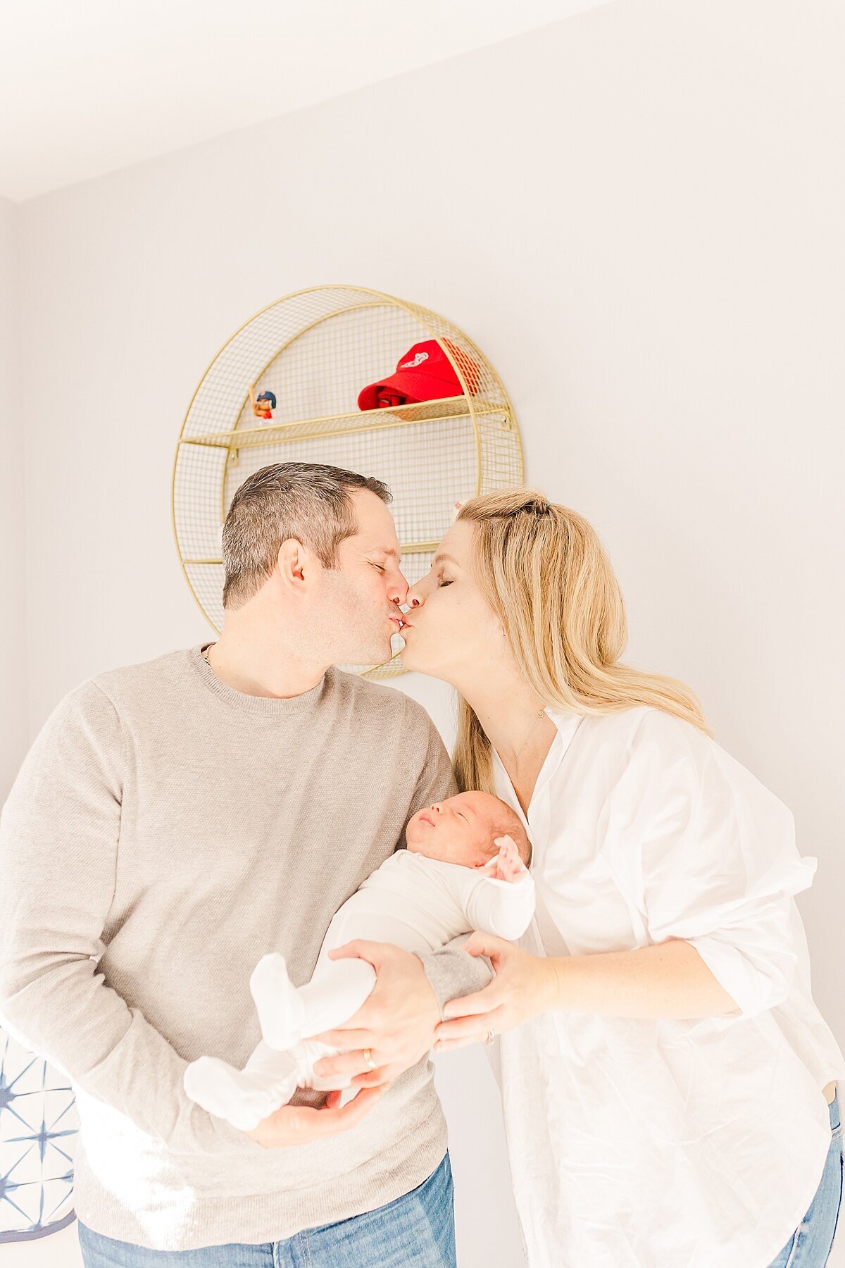 parents hold baby and kiss  during in home newborn photo session with Sara Sniderman Photography in Sherborn Massachusetts