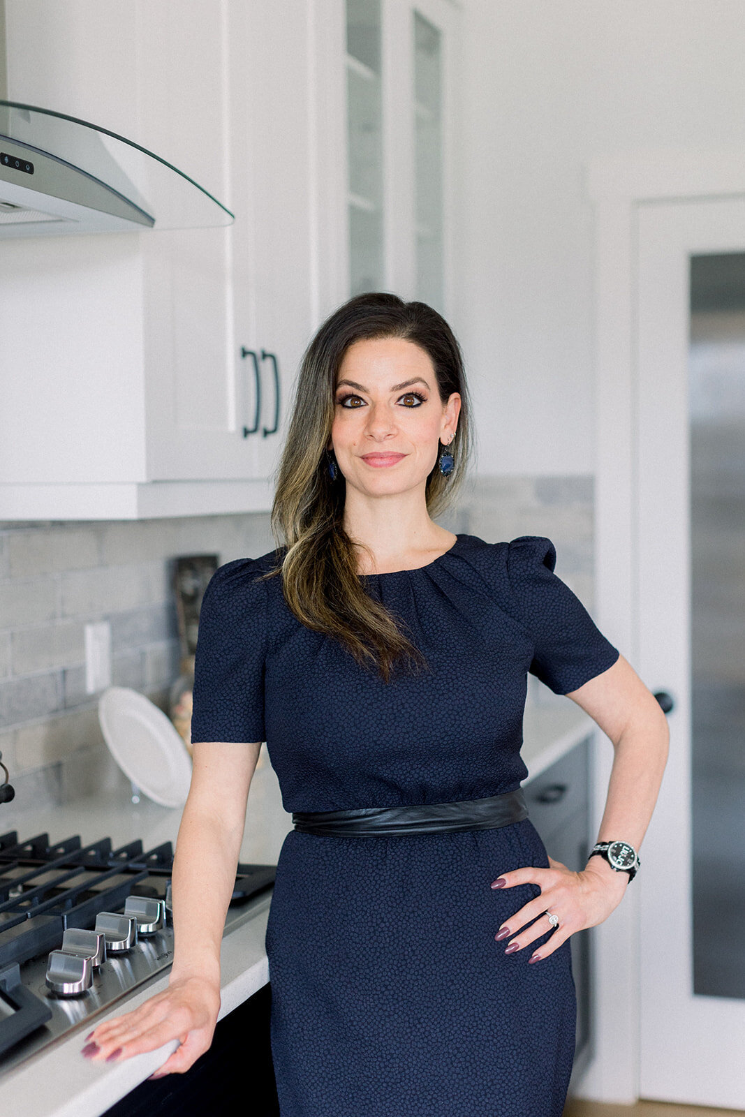 Woman with dark hair confidently standing with one hand on hip in a light and airy kitchen