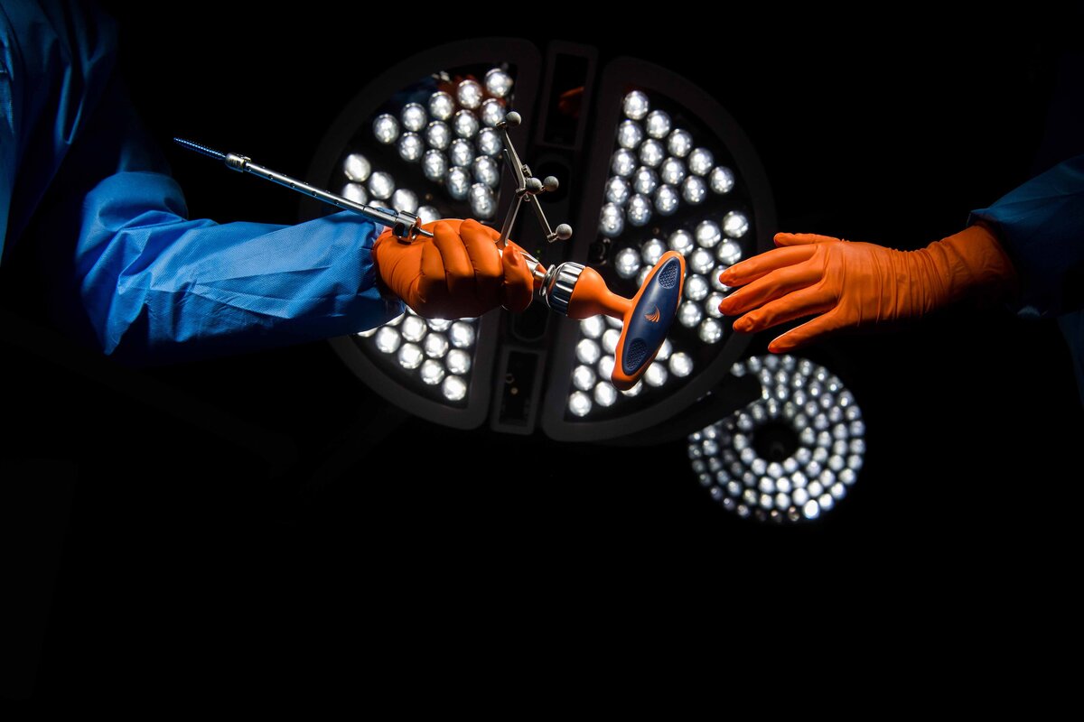 A surgical tool is handed off to a surgeon during a surgery with the operating room light in the background