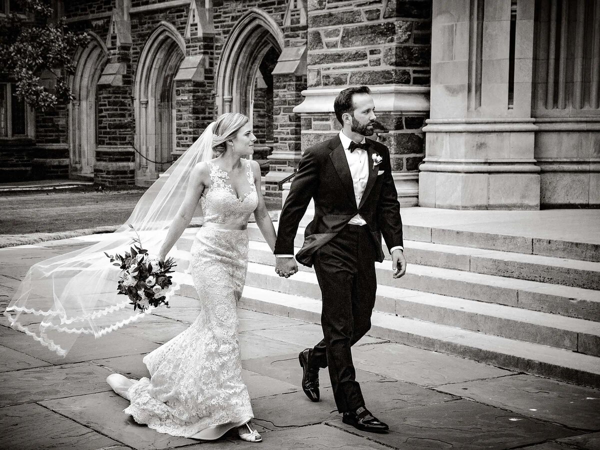 Bride and groom walking hand in hand in front of a gothic-style building