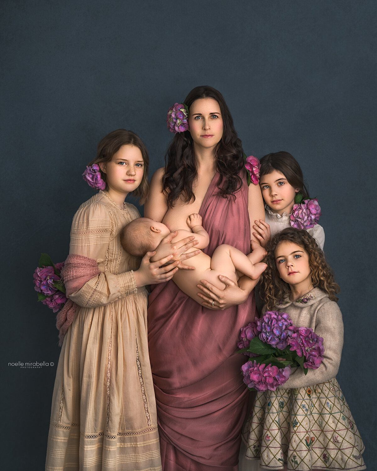 Mother and her four girls in pinks and neautral colours, holding flowers.